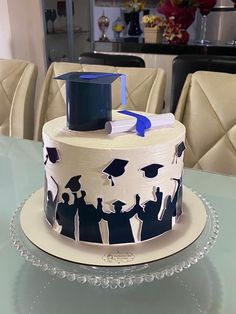 a decorated cake on a glass table with people in graduation caps and gowns around it