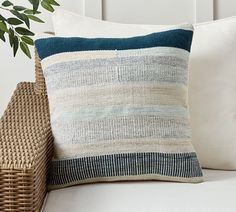 a close up of a pillow on a bed near a basket with a plant in it