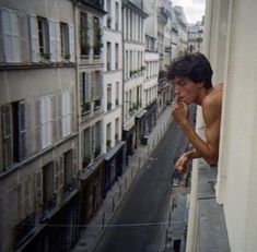 a shirtless man standing on the ledge of a building looking out at an alleyway