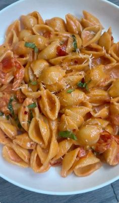 a white bowl filled with pasta and sauce on top of a wooden table next to a fork