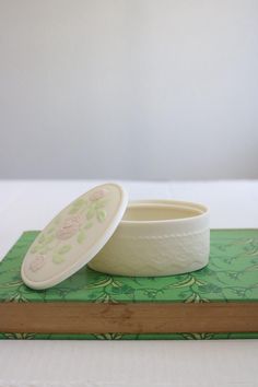 a white bowl sitting on top of a green book next to a cup with lid