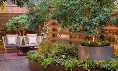 an outdoor seating area surrounded by plants and trees with wooden slats on the wall