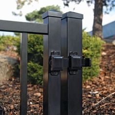 a black gate with two latches on it in front of some bushes and trees