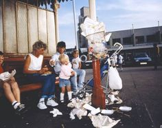 a group of people sitting on top of a wooden bench next to a pile of trash