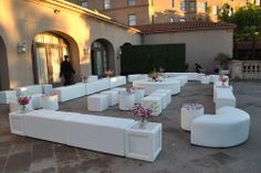 an outdoor seating area with white couches and flowers in vases on the ground