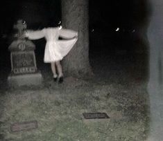 a woman standing in front of a grave at night with her arms spread wide out