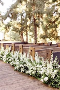 white flowers are lined up along the side of pews at an outdoor wedding ceremony