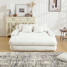 a large white couch sitting on top of a wooden floor next to a dresser and table