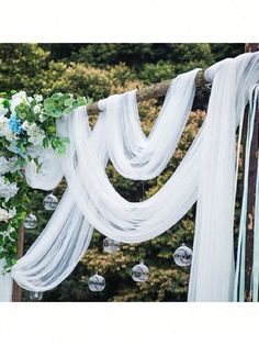 an outdoor wedding ceremony with white drapes and flowers on the back droplet, hanging from a tree branch