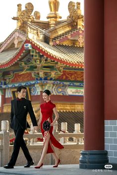 a man and woman are walking in front of a chinese building with red columns on either side