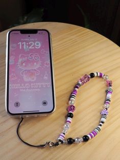 a cell phone on a table next to a beaded necklace with an hello kitty theme