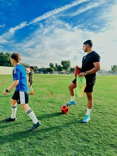 two soccer players are on the field with their balls and gloves in hand, while another player is about to kick it