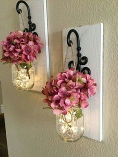 two mason jars with flowers are hanging on the wall next to each other, both holding lights