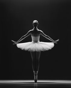 a black and white photo of a ballerina wearing a tutu in front of a dark background