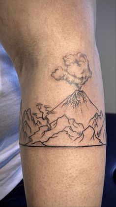 a man with a tattoo on his leg that has a mountain and clouds in the sky