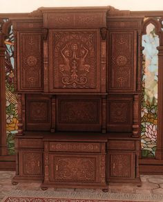 an intricately carved wooden cabinet in front of stained glass windows with flowers on the wall