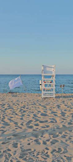 a white chair sitting on top of a sandy beach next to the ocean under a blue sky