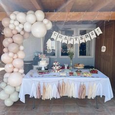 a table topped with lots of white balloons next to a cake and cupcakes