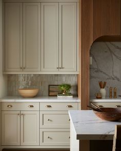 a white kitchen with marble counter tops and wooden cabinetry, along with a bowl on the island