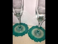 two wine glasses sitting next to each other on top of a table with green coasters