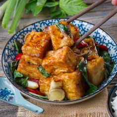 a bowl filled with tofu and vegetables next to chopsticks on a table