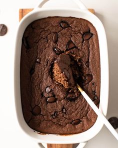 a chocolate cake in a white casserole dish with a spoon sticking out of it