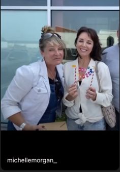 two women standing next to each other in front of a building