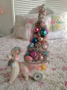 a white teddy bear sitting on top of a bed next to a small christmas tree