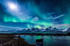 the aurora bore is shining brightly in the night sky over water and mountains with snow on them