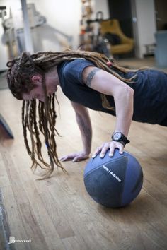 a man with dreadlocks is doing push ups on a medicine ball