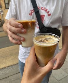 two people are holding drinks in their hands on the side walk while one person is wearing a white t - shirt