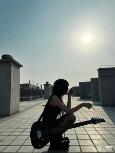 a woman sitting on the ground with an electric guitar in her hand and looking up at the sky