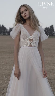 a woman standing in a field wearing a wedding dress with short sleeves and an open back