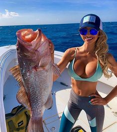 a woman holding a large fish while standing on a boat