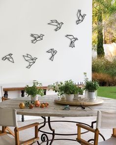 an outdoor table with chairs and potted plants on it in front of a white wall