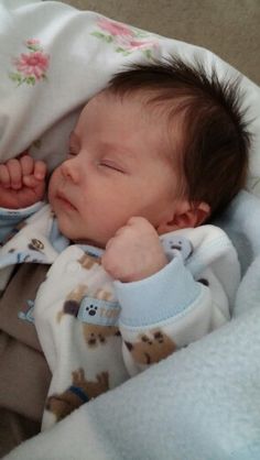 a baby is sleeping in a blanket with his head resting on his hand and eyes closed