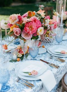 the table is set with blue and white plates, silverware, and pink flowers