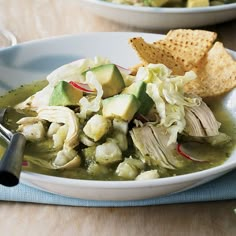 a white bowl filled with green soup and some crackers on the plate next to it