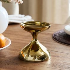 a gold candle holder sitting on top of a wooden table next to plates and flowers