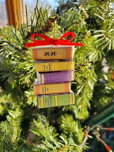 a christmas ornament made out of books hanging from a pine tree with a red ribbon