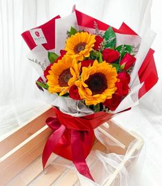 a bouquet of sunflowers and roses wrapped in red ribbon on a wooden box