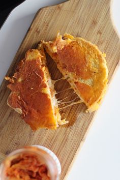 a wooden cutting board topped with two pieces of food next to a jar of sauce