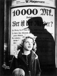 a black and white photo of a woman standing in front of a poster with the shadow of a man on it