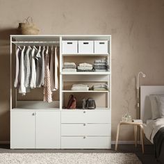 an open closet with clothes and shoes on shelves next to a bed in a bedroom