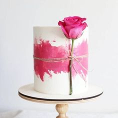 a white and pink painted cake with a single rose on the top that is tied up