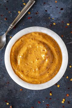 a white bowl filled with sauce next to a spoon on top of a blue surface