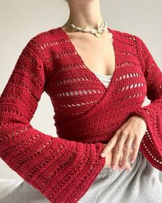 a woman wearing a red knitted cardigan sitting on a white couch with her hands in her pockets