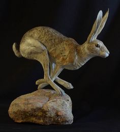 a statue of a rabbit sitting on top of a rock next to a black background