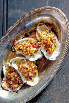 three oysters with white sauce and crumbs in a silver dish on a wooden table