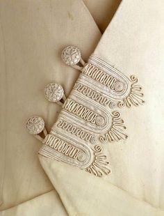 an embroidered white jacket with buttons on the lapel and two matching cufflinks